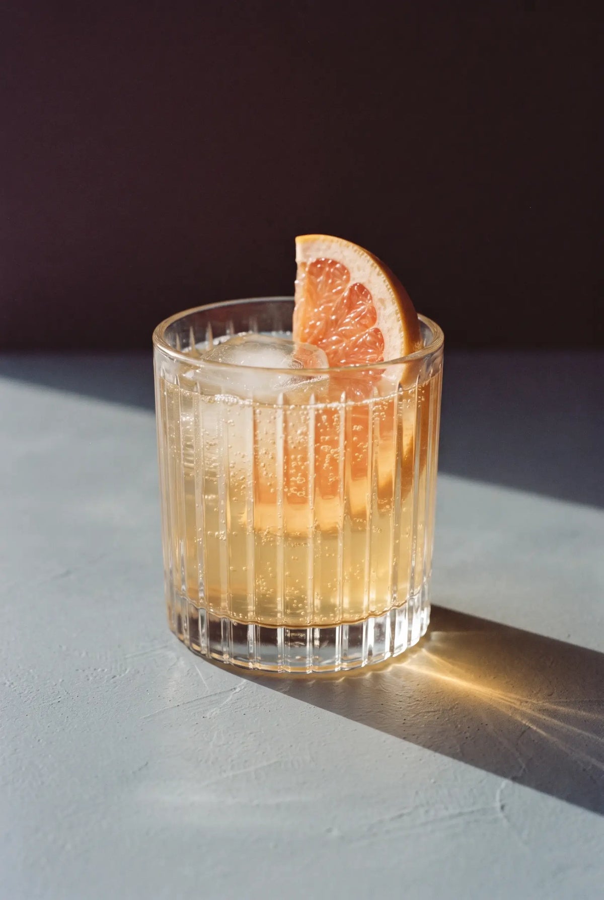 Kinn and Grapefruit: a short ribbed tumbler of Kinn over one big cube with a pink grapefruit wheel